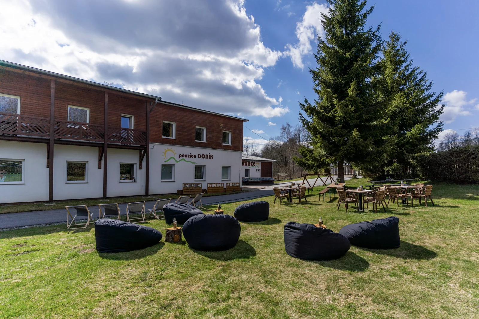 Resort Pasečná – Celkový exteriér resortu s venkovním posezením na trávníku.